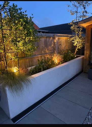 Customer's garden at dusk, with plants in a raised bed warmly illuminated by LED spike lights.