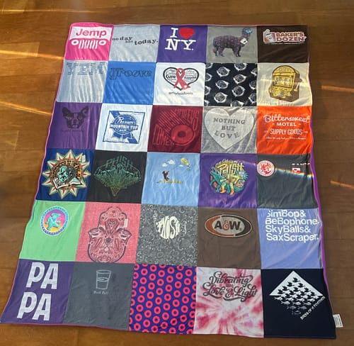 Customer's colorful Project Repat T-Shirt Quilt made from many different shirts, spread out on a wooden floor.