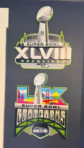 Reviewer's two Seattle Seahawks 3D metal wall art signs, including the Super Bowl XLVIII version, hung on a dark wall.