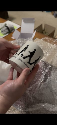 Customer holding their white ceramic BTS - ARIRANG OFFICIAL MD MUG with a black silhouette design.