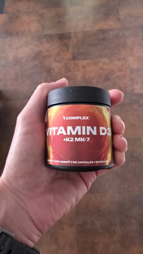 Customer's hand holding a small black bottle of Complex Vitamin D3+K2 MK-7.