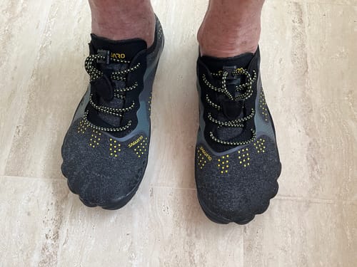 A customer wearing the dark grey Fast Ⅰ Aqua Barefoot Water Shoes with yellow accents on a tiled floor.