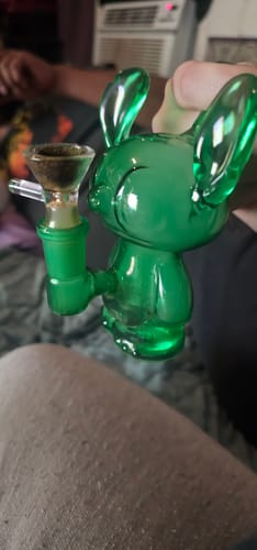 A customer holds the cute, green Small Friend Glass Bong, showing its character design and attached bowl.