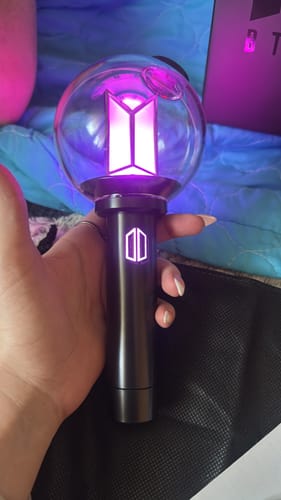 Customer holding the BTS Official Light Stick Ver.4, which is illuminated and glowing with a purple light.