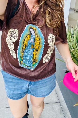 Reviewer wearing the brown mesh Brown Blessings Jersey with Our Lady graphic, paired with denim shorts.