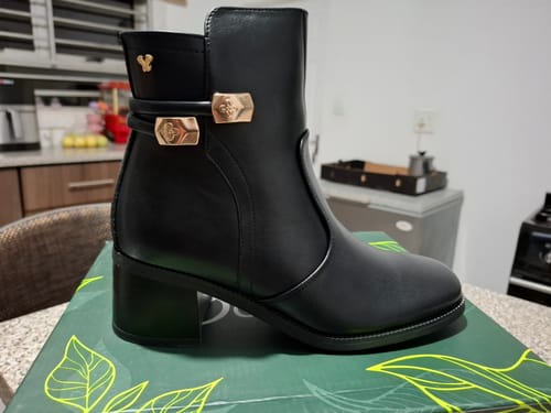 Customer's black Butterfly Feet Nikah 2 Ankle Boots with gold metal trim, displayed on its box.