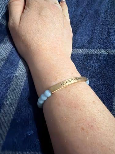 Reviewer's custom Blue Angelite bracelet on their wrist, engraved with the words 'HYDRO HERO'.