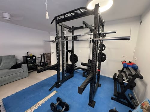 Ein Kunde zeigt die kompakte HellHound Hantelablage, die in einem Heimstudio neben einem Power-Rack steht.