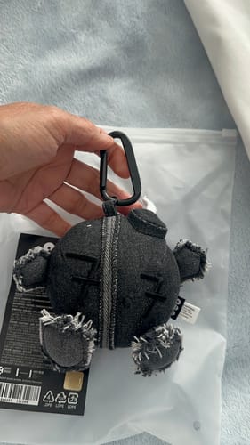 Customer holding the dark, frayed fabric ARMY BOMB PLUSH KEYRING by its black carabiner clip.