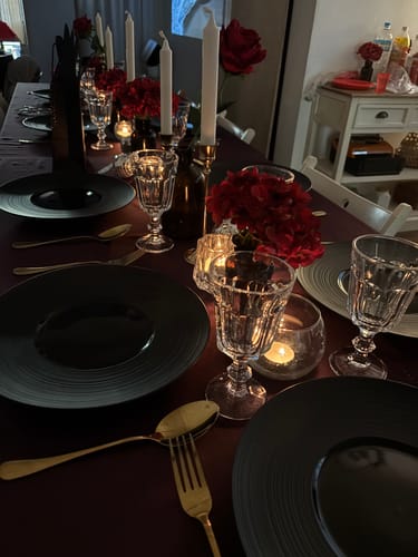 Customer's elegant dinner table set for the Masquerade Ball Murder Mystery game with dark plates and red decor.
