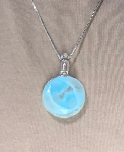 Close-up of a customer wearing a circular, light blue Glow in the Dark Pendant on a silver chain.