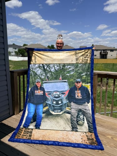 Customer holding up a large custom collage blanket with a photo of a couple in front of an off-road vehicle and a blue border.