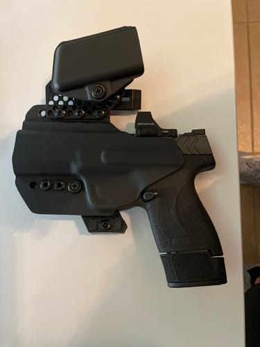 Customer's black APX holster holding a handgun with a red dot sight and an attached magazine carrier, on a white surface.