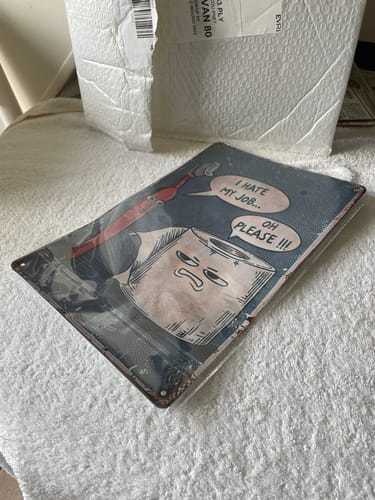 Customer's "I Hate My Job" funny wall art, which arrived bent, still in its plastic wrap next to the shipping envelope.