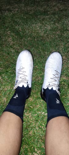 Un client porte le Maintien de Compression pour Chevilles avec des chaussures de football sur un terrain en herbe.