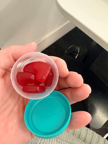 Customer holding several red, heart-shaped Strawberry Hormone Gummies in a small clear cap.