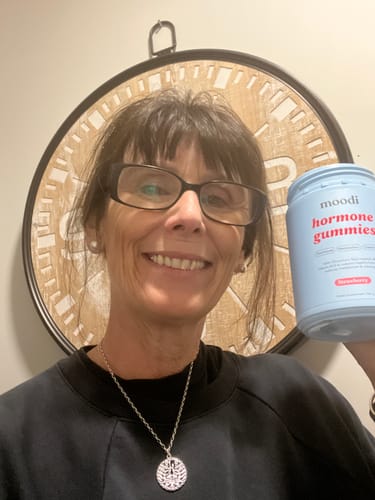 Customer smiling while holding a blue jar of moodi hormone gummies.