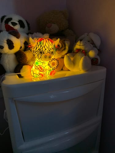 Customer's glowing Highland Cow LED Night Light on a white dresser with several stuffed animals.