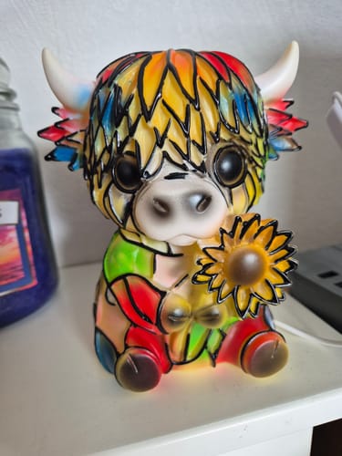 Customer's colorful Highland Cow night light holding a sunflower, shown unlit on a white surface.