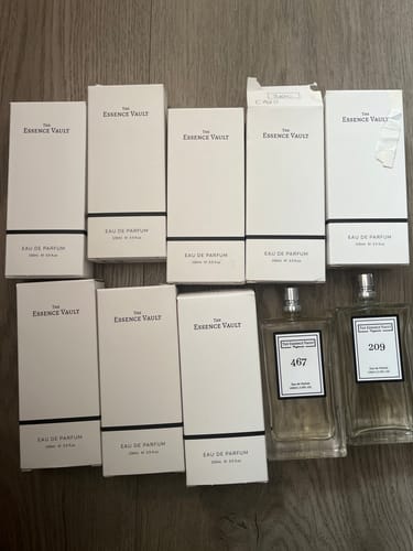 Reviewer's collection of The Essence Vault perfumes, with multiple white boxes and two used bottles on a wooden surface.