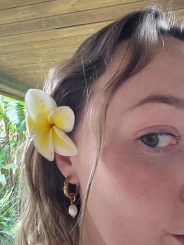 Close-up of a reviewer wearing the gold Bethany Pearl Drop Hoop earring, with a flower tucked behind their ear.