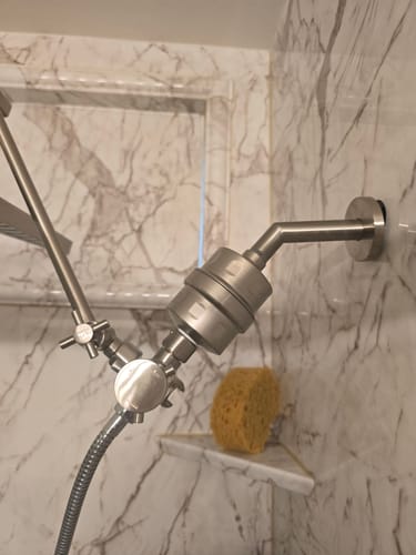 Customer's brushed metal shower filter installed in a modern, marble-tiled shower.