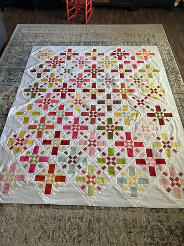 Customer's finished Positive Vibes quilt top with colorful X-blocks laid out flat on a rug.