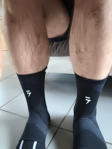 Un client portant les maintiens de compression pour chevilles V3 noirs aux deux pieds en position assise.