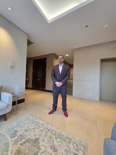 Client portant le pantalon WESSON-FARRELL rouille dans un hall, assorti à un veston.