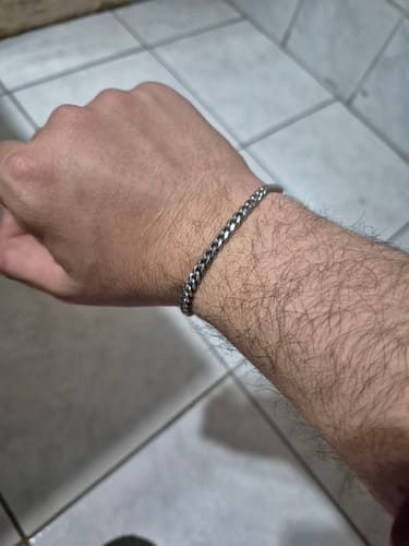 Cliente mostrando la Pulsera Miami Cuban de 5mm en su muñeca sobre un suelo de baldosas.