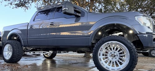 Customer's lifted gray Ford F150 with the white Traction Bar Kit installed, viewed from the side.