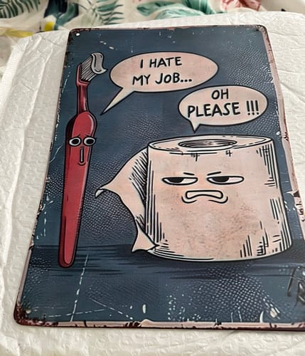 Customer's 'I Hate My Job' metal wall art sign with a cartoon design lying flat on a cushioned surface.