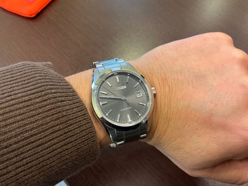 Primer plano del reloj Citizen NB1050-59H en la muñeca de un cliente, mostrando su esfera gris.