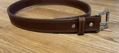 Customer's brown Montana Bison belt coiled on a wooden surface, showing the double stitching and steel buckle.