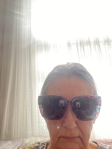 A reviewer wearing the oversized floral frame fit over sunglasses indoors.