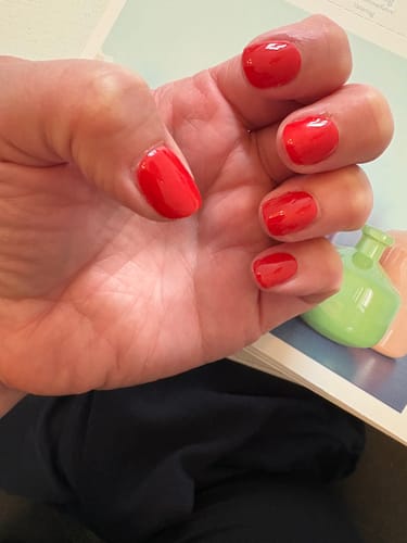 Die Hand einer Kundin mit glänzenden, roten „Hot Date“ UV-Gel-Folien auf kurzen Nägeln.