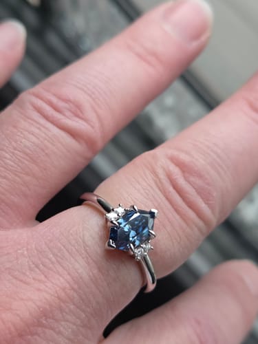 Customer's hand wearing a Dutch marquise engagement ring with a blue moissanite stone and pave accents.