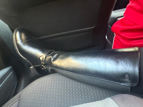 Customer wearing the black Miss Black Earth 1 High Boots, showing the close fit on their leg while seated in a car.
