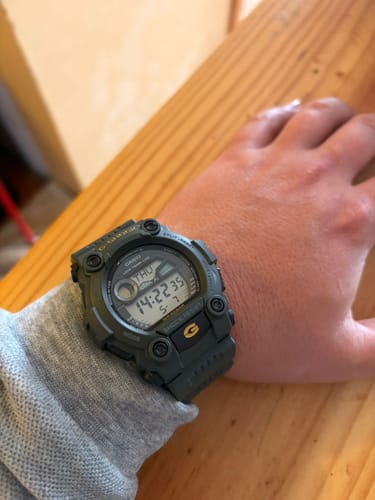 Cliente mostrando su reloj Casio G-Shock Verde Militar en la muñeca en un ambiente interior.