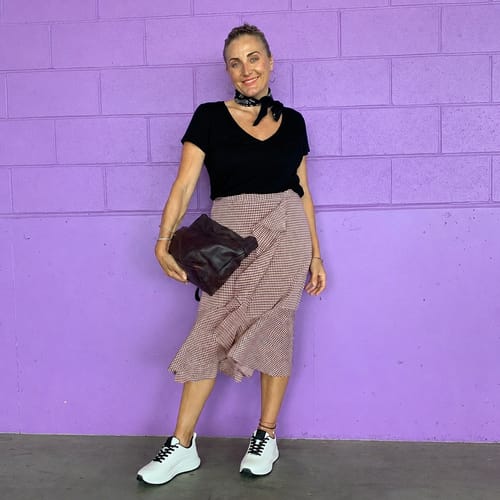 A customer models their white CloudStep™ sneakers, pairing them with a patterned skirt and a black top.