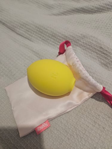 Reviewer's yellow Lem Clitoral Massager resting on its white satin storage pouch.