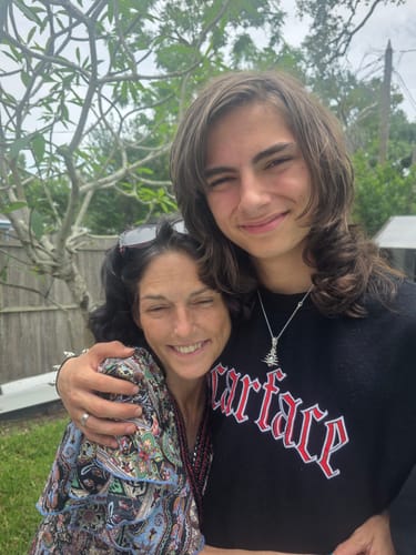 Reviewer wearing the silver 1M MYSTERY PENDANT on a necklace while hugging another person outdoors.