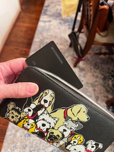 Customer holding a wallet with a dog print, showing the black SPOTMINDERS Tracking Card in a zip pocket.