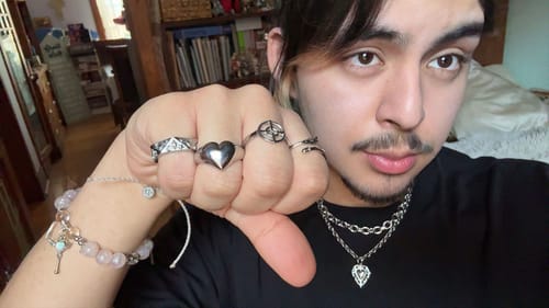 Reviewer wearing the chunky Heart Ring on their middle finger, styled with several other rings and jewelry.