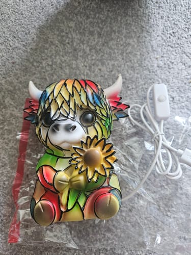 Reviewer's colorful Highland Cow LED Night Light shown unlit on a gray surface next to its power cord.