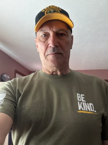 Reviewer wearing the olive green Be Kind t-shirt, with 'BE KIND.' in white and yellow text on the chest.