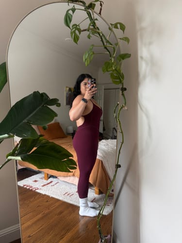 Reviewer showing the slim-leg fit of The Bare Onesie in black-cherry with a side-profile mirror selfie.