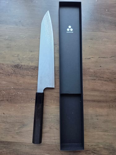 Reviewer's Nigara Hamono Gyuto displayed on a wooden surface next to its sleek black presentation box.