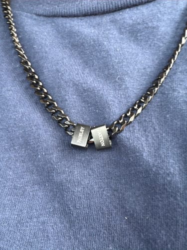 Customer wearing the Legacy necklace, showing two dark, engraved beads on a chain against a blue shirt.