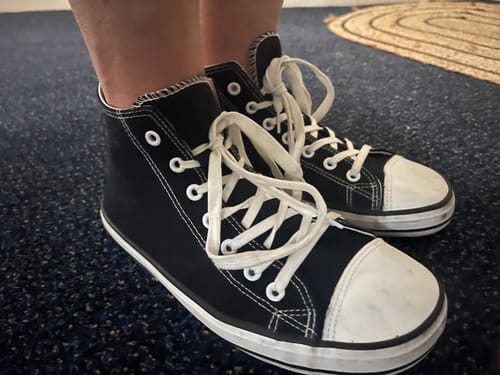 Reviewer wearing the black Roam I - Barefoot Shoes, showing a side view on a dark carpet.